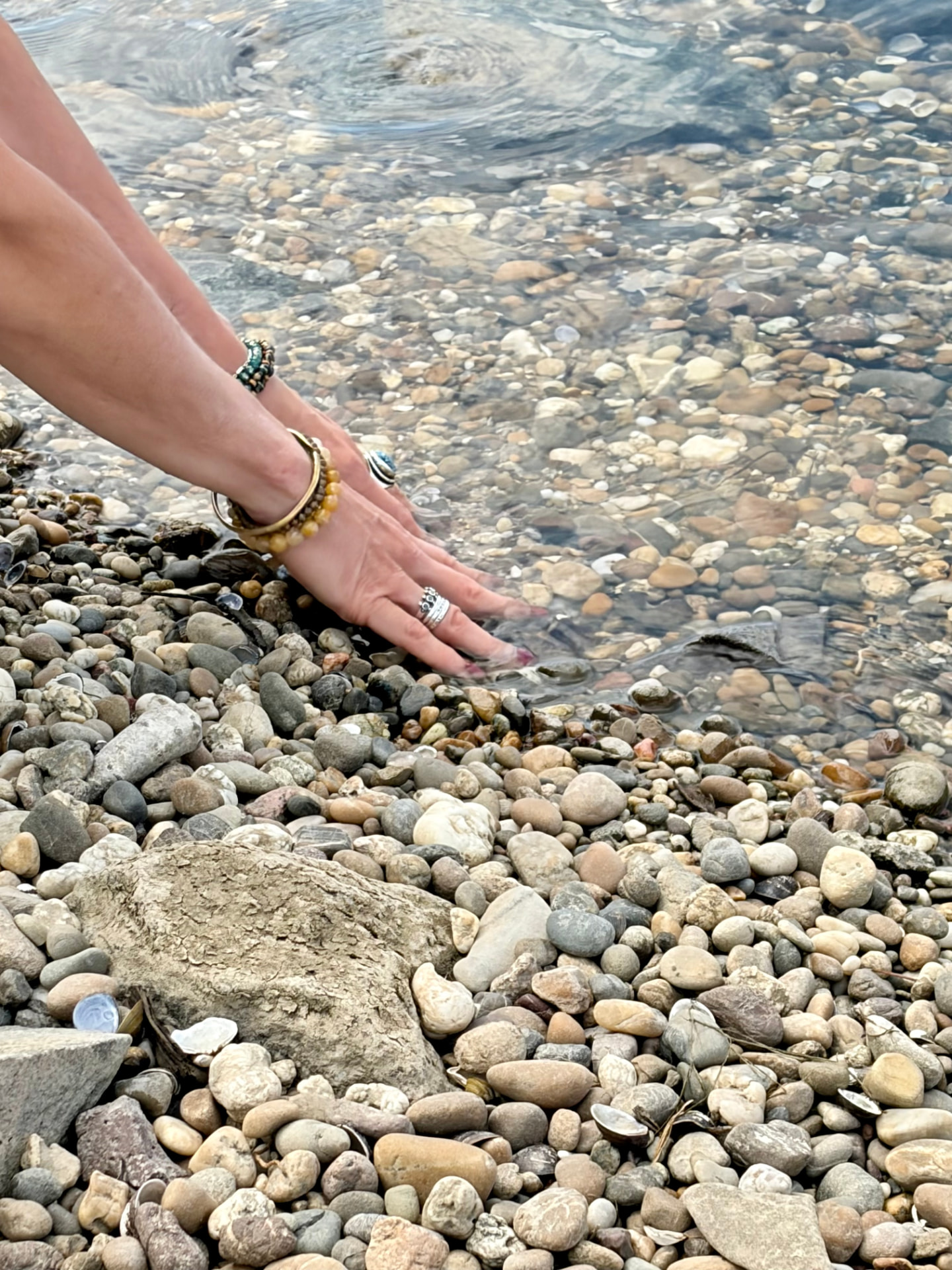 A hand resting in clear river water over smooth stones
